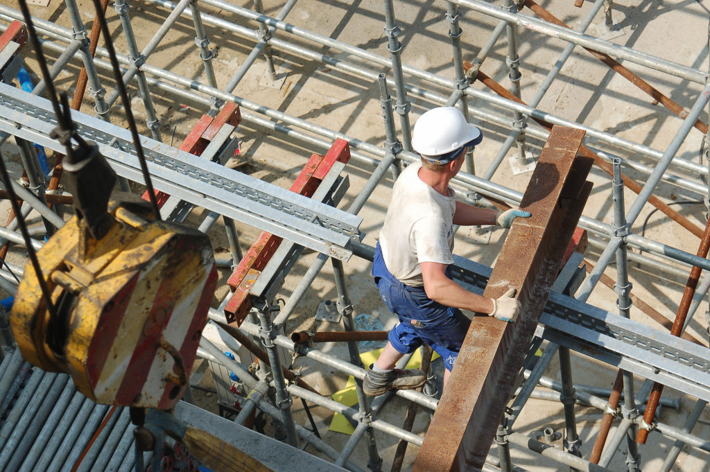 Construction worker unloading steel beam on scaffolding